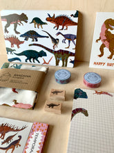 Laden Sie das Bild in den Galerie-Viewer, selection of Dino related products from jungwiealt, showing organic cotton bandana, breakfast plate, wooden stamps, notepad, temporary tattoos, washi tape and postcard